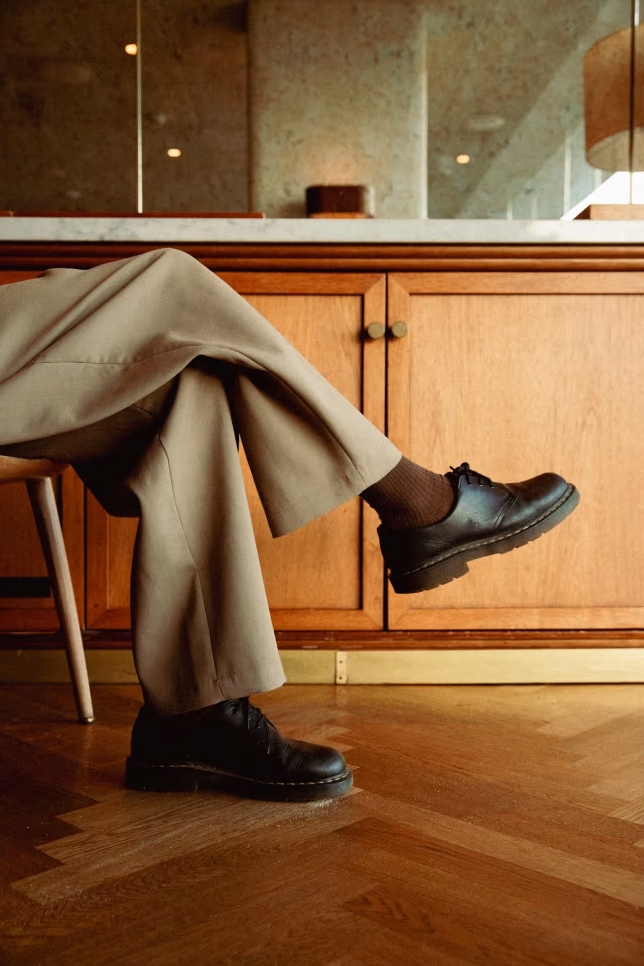 Person in brown trousers sitting on chair, wearing black shoes in a stylish office setting.