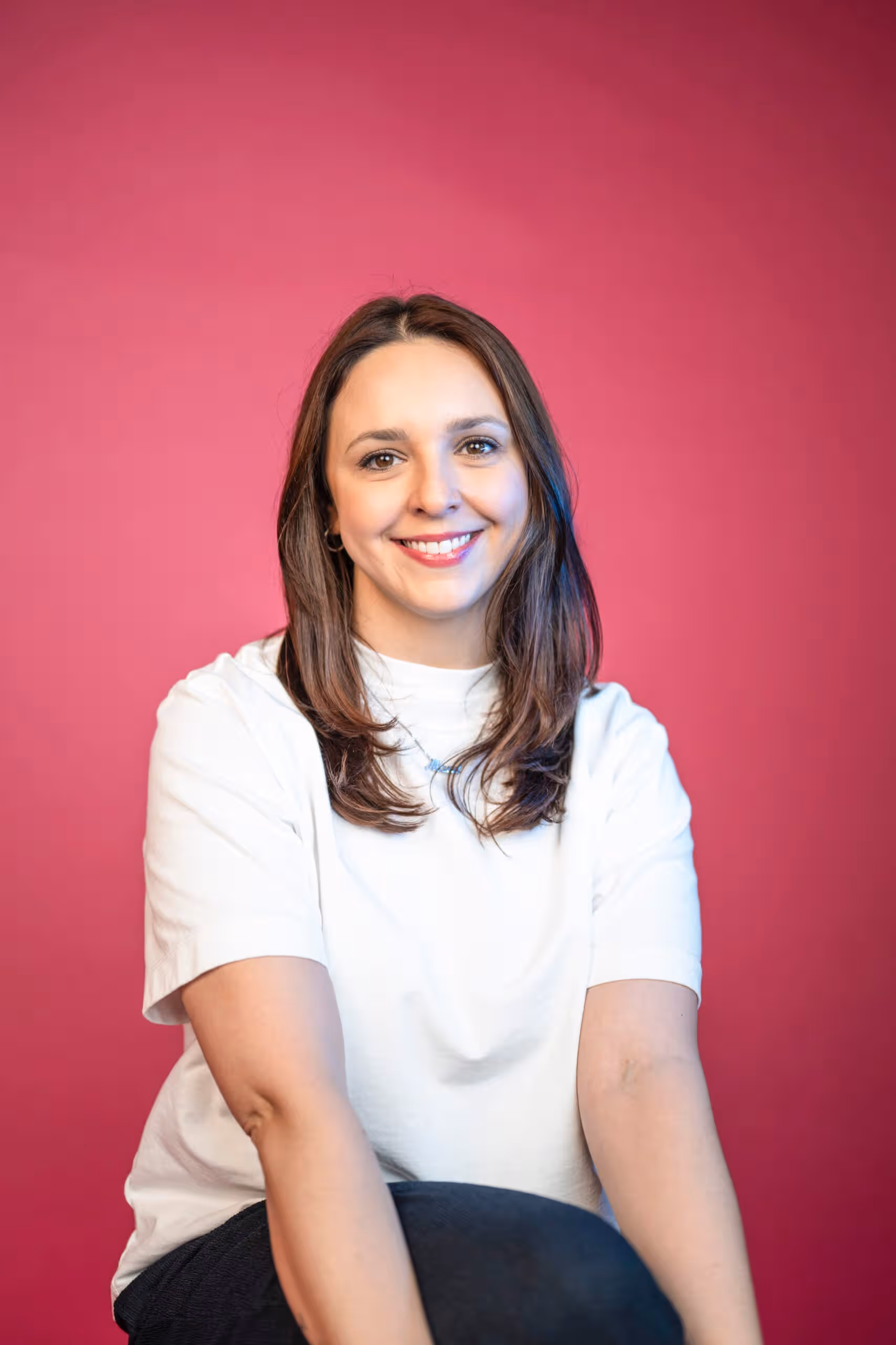 Professional marketing team member with dark hair in studio headshot wearing white shirt against pink background