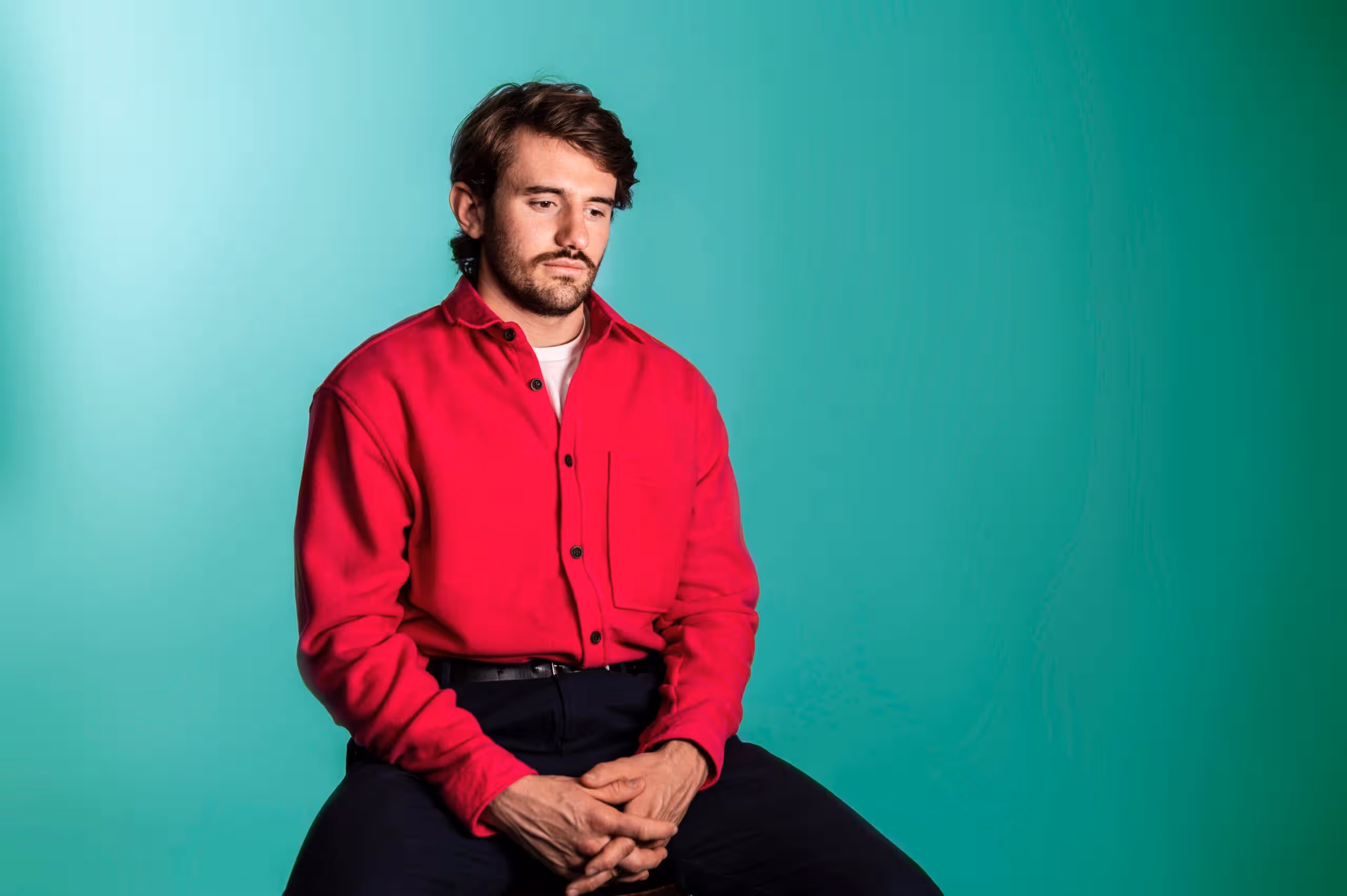 Man in red shirt sitting against turquoise background, representing team member at Salience marketing agency.