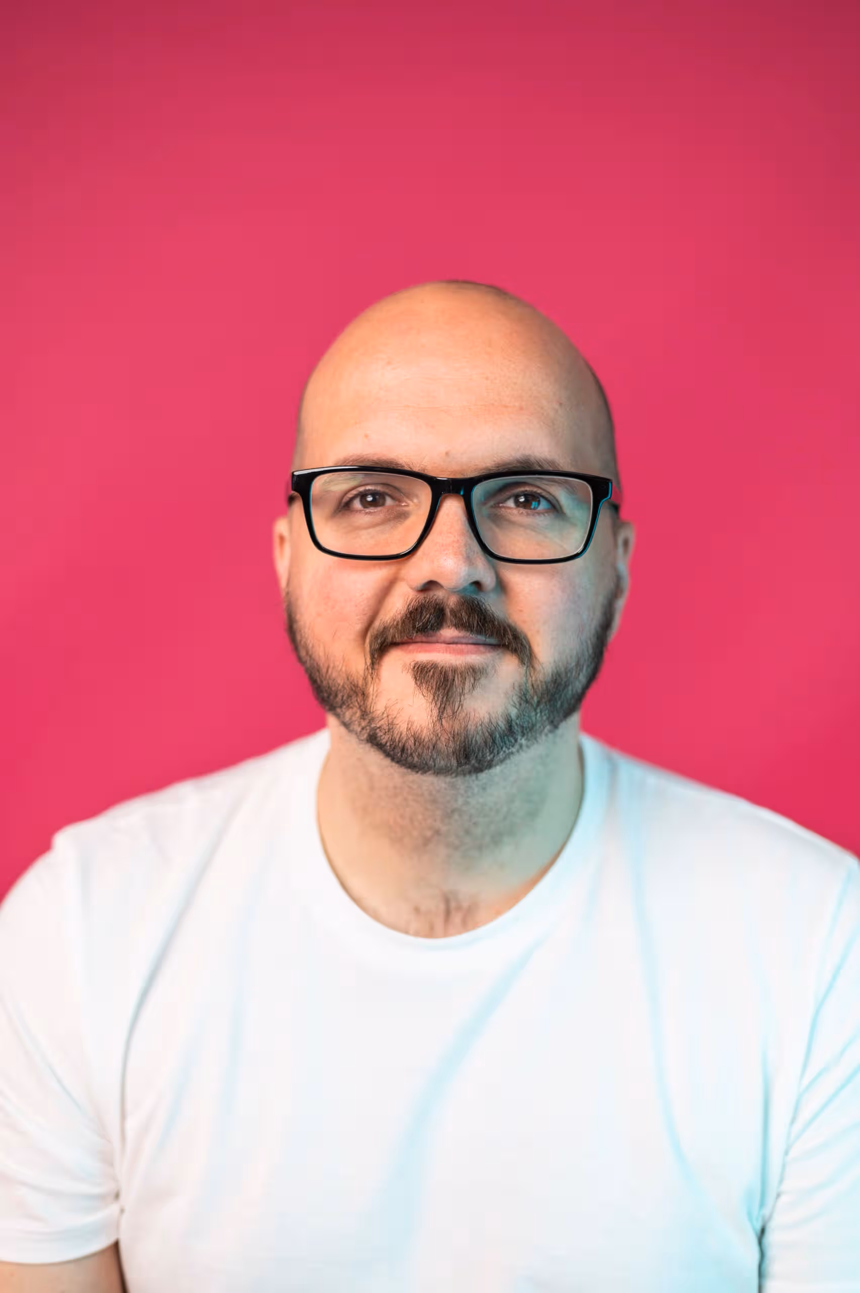 Male professional with glasses wearing white shirt against pink studio background