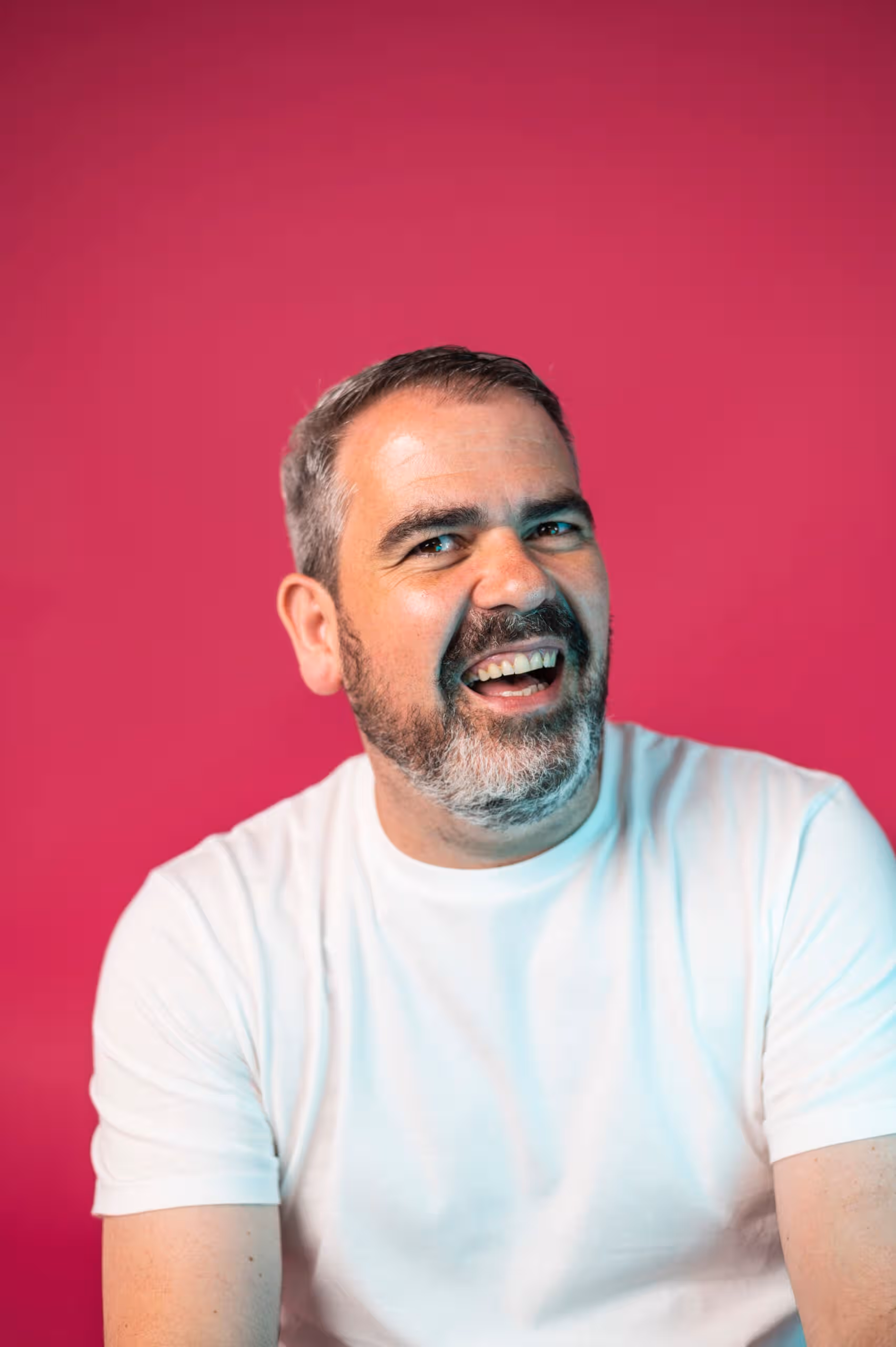 Bearded man in white t-shirt smiling, marketing team headshot