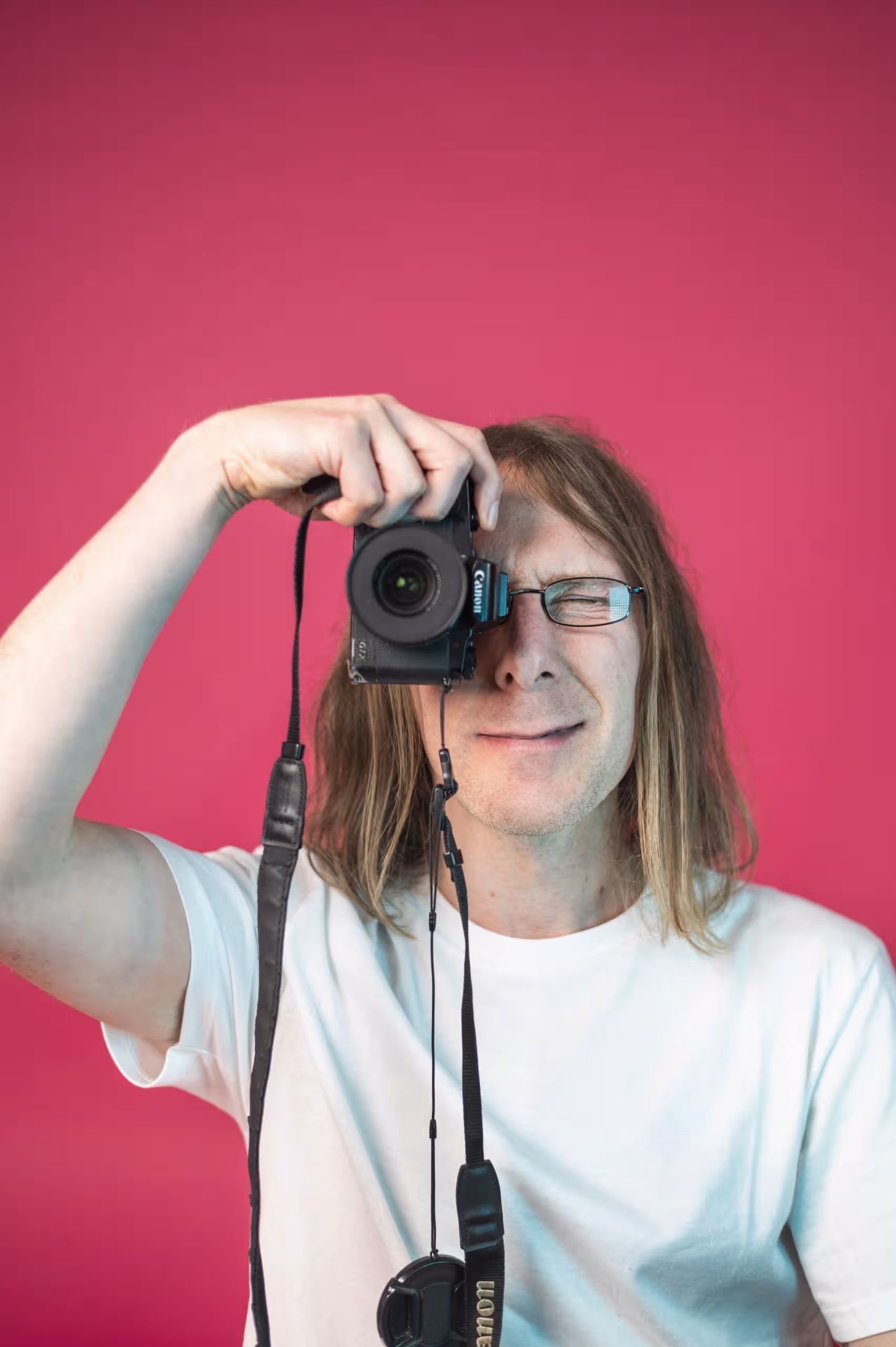 Man with a camera against a pink background in creative marketing setting.