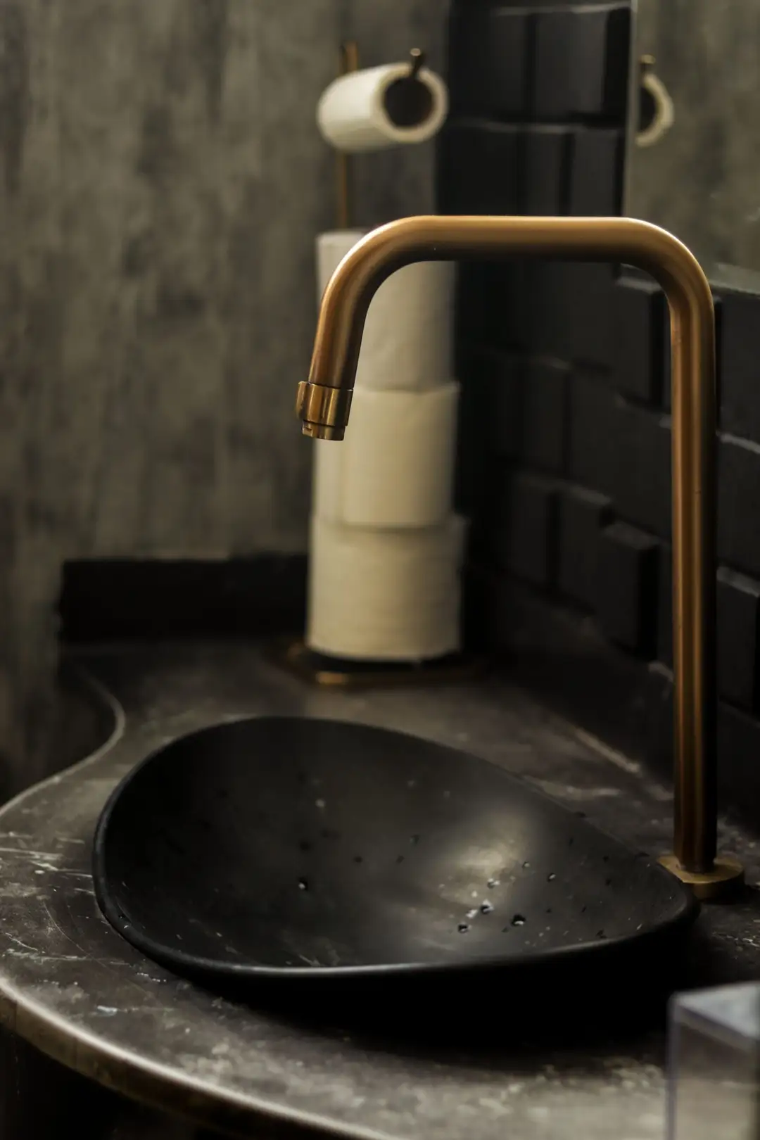 A modern bathroom sink with a sleek black basin and brass faucet, complemented by a stylish interior design. (Photo: Guilherme SimĂŁo via Pexels)