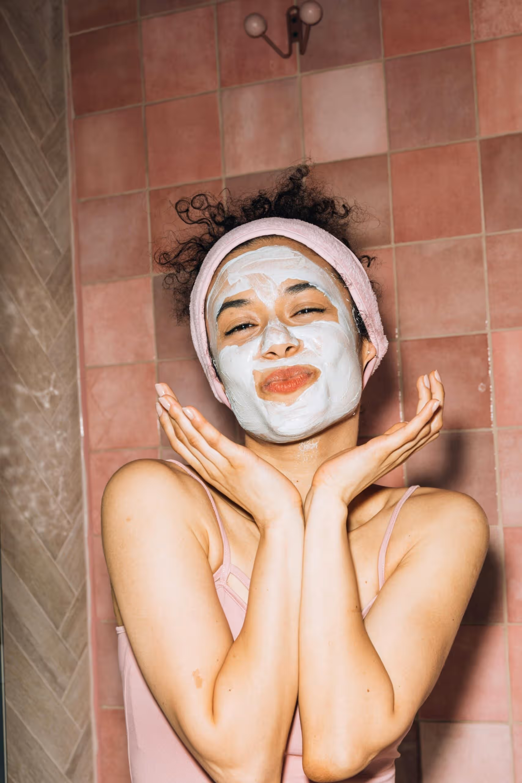 Woman wearing white skincare mask with hands near face in bathroom